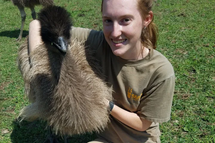 a woman holding a teddy bear sitting on top of a grass covered field
